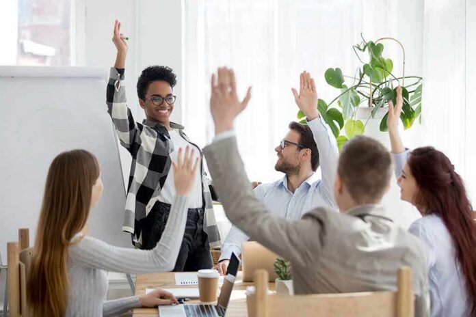Team in meeting raising hands around a smiling presenter