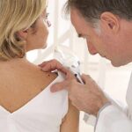 Melanoma Rebounds Crushed By Custom Shot Doctor examining a patients skin with a magnifying glass