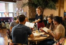 Wage War Collides With Vanishing Paychecks Server taking orders from a group at a restaurant table