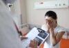 Woman covering her face while doctor holds a clipboard in a hospital room