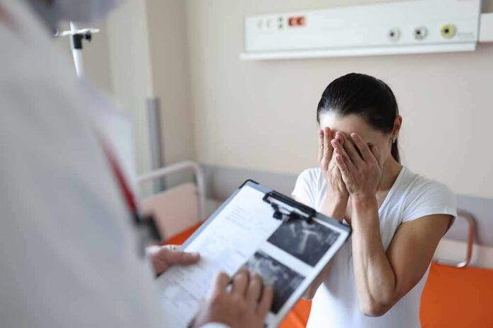 Woman covering her face while doctor holds a clipboard in a hospital room