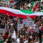 Crowd of protesters holding signs and a large tricolor flag