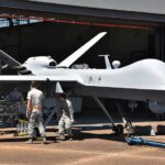 Military drone being serviced by ground crew outside a hangar