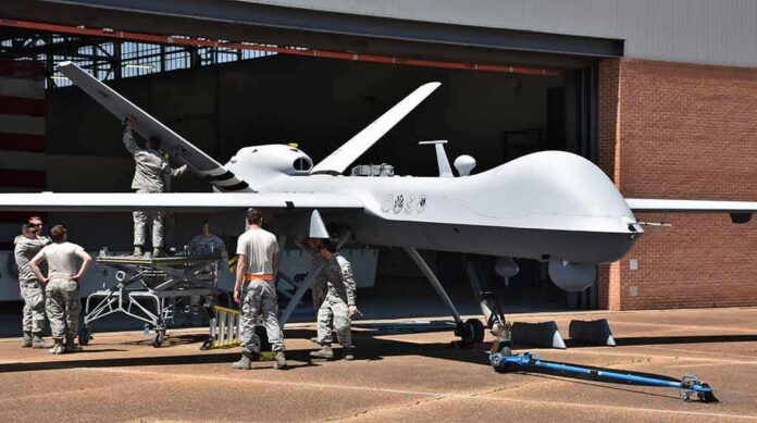 Military drone being serviced by ground crew outside a hangar