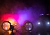 Handcuffs on a surface with police cars and flashing lights in smoky darkness