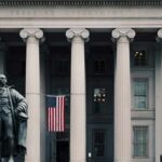 Statue in front of a neoclassical government building with columns and a U.S. flag