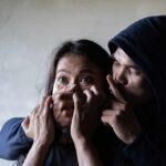 woman being restrained by a hooded person