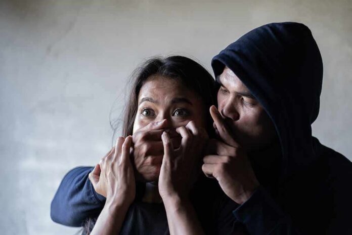 woman being restrained by a hooded person