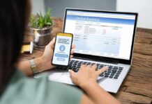 Person using smartphone to approve bank transfer beside laptop with online banking