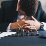 Businessman with head down behind stacks of coins and downward arrow