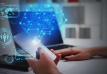 Hands using smartphone near laptop with digital hexagon interface overlay