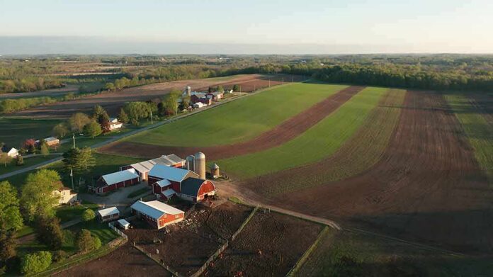 Aerial view of a farm with red barns and expansive green and brown fields