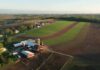Aerial view of a farm with red barns and expansive green and brown fields