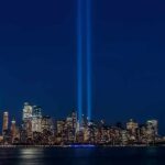City skyline at night with twin blue light beams rising into the sky