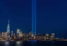 City skyline at night with twin blue light beams rising into the sky