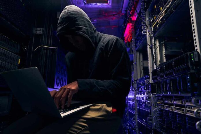 Hooded person using a laptop in a dark server room