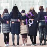 Group of women standing arm in arm with purple ribbons