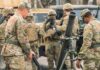 Soldiers in camouflage gather around a mortar during field training