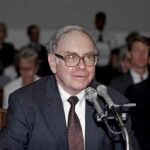 Older man in suit speaking at microphones during hearing