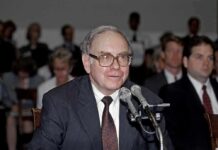Older man in suit speaking at microphones during hearing