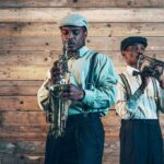 Two jazz musicians play saxophone and trumpet against a wooden wall