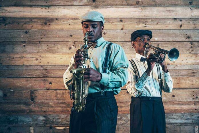 Two jazz musicians play saxophone and trumpet against a wooden wall