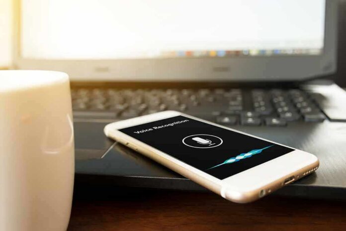 Smartphone with voice assistant on screen beside laptop and coffee mug