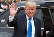 Donald Trump waves while standing beside a black vehicle