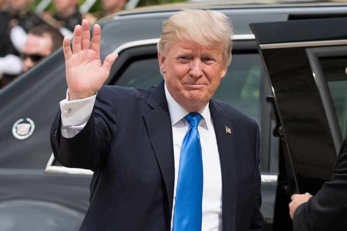 Donald Trump waves while standing beside a black vehicle