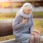 Older woman on park bench holding chest
