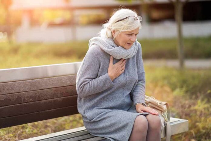 Older woman on park bench holding chest