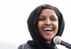 Ilhan Omar smiling while speaking at a microphone