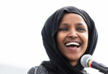 Ilhan Omar smiling while speaking at a microphone