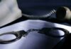 Handcuffs on a document beside a coiled telephone handset