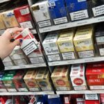 Hand selecting a pack of cigarettes from a store shelf
