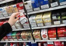 Hand selecting a pack of cigarettes from a store shelf