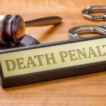 Gavel, handcuffs, and a nameplate reading death penalty on a wooden desk