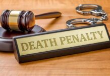 Gavel, handcuffs, and a nameplate reading death penalty on a wooden desk