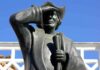 Bronze statue of a historical figure saluting against a blue sky