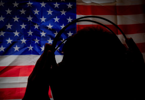 Silhouette with headphones against American flag background.