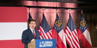 Man speaking at "The Florida Blueprint" event with flags.