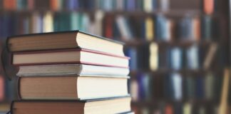 Stack of books on table with blurred bookshelf background.