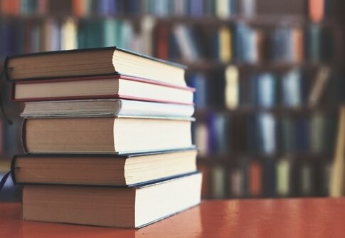 Stack of books on table with blurred bookshelf background.