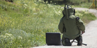 Bomb squad personnel in protective gear working on device.