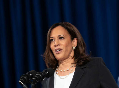 Woman speaking at a podium with blue background.