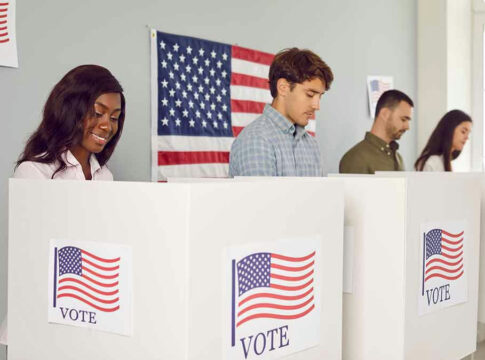 People voting in booths with American flags.