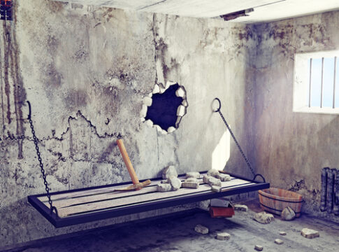 An abandoned prison cell with a broken wall and a makeshift bed
