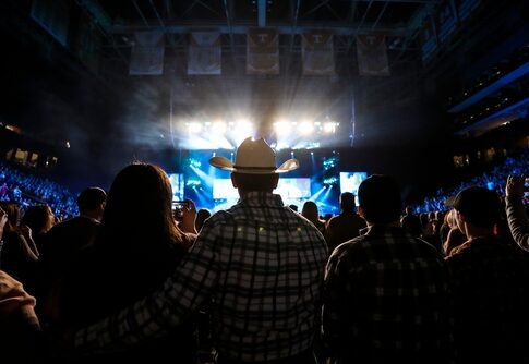 Audience at a concert with bright stage lights and a cowboy hat in the foreground