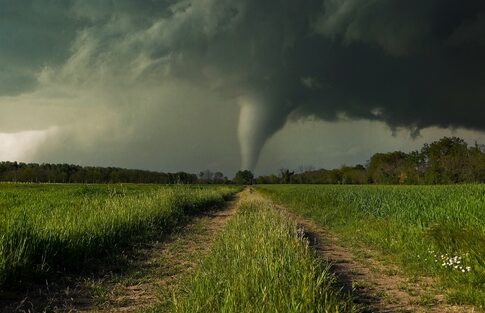A tornado forming in a rural landscape under dark storm clouds