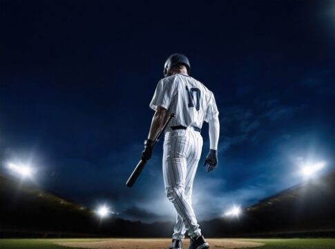 A baseball player standing on the field at night, holding a bat